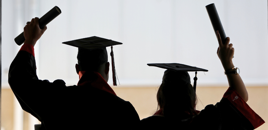 两名威斯康星大学毕业生背对镜头，举着毕业证书庆祝
